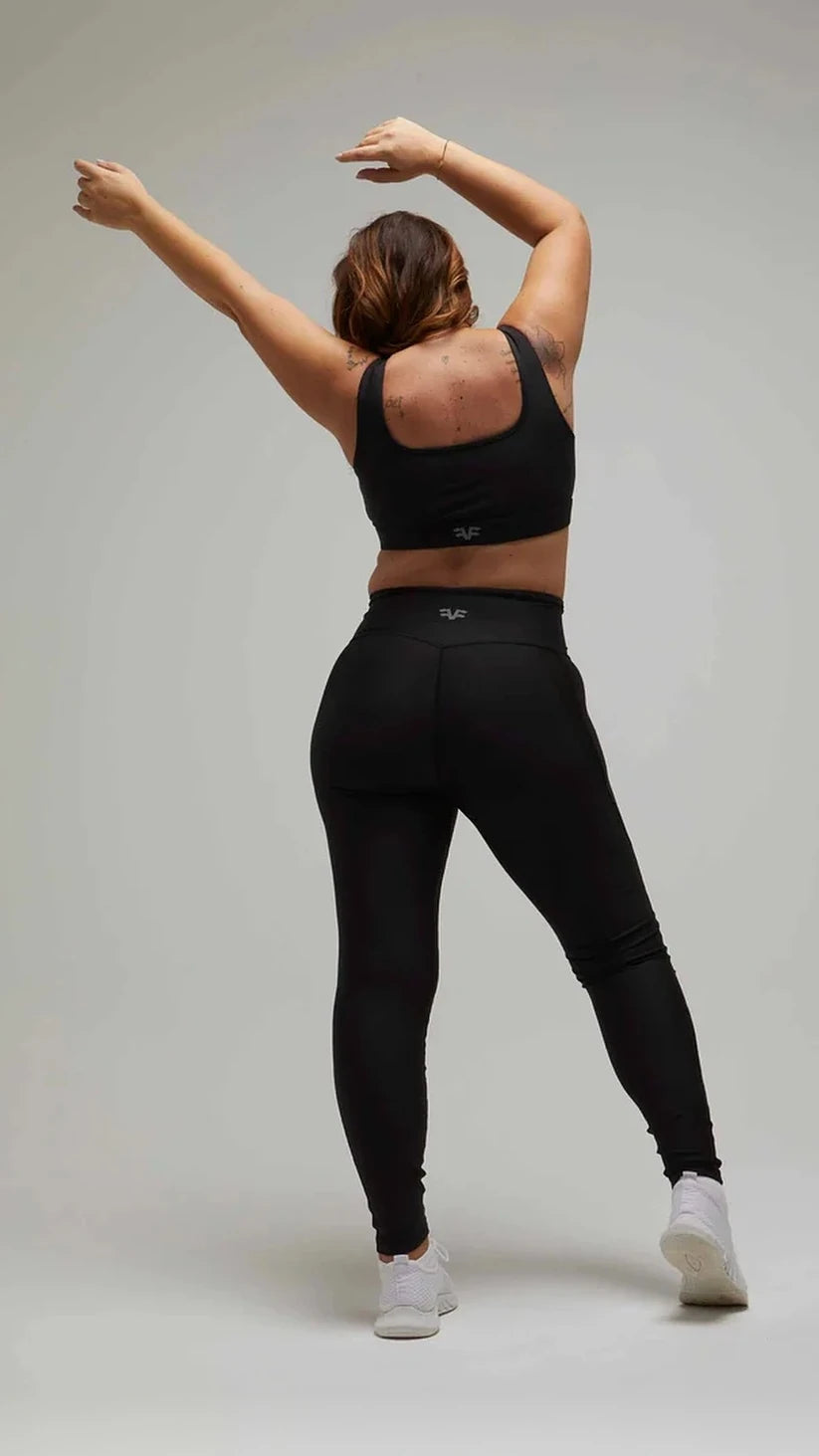 Modella di spalle con completo sportivo nero Flexivel, leggings a vita alta e top, braccia alzate