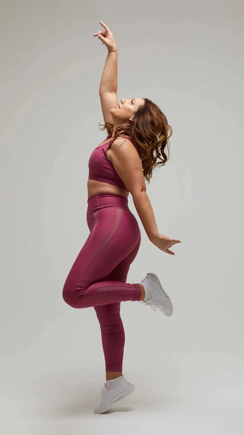 Modella con completo sportivo prugna Flexivel in posa dinamica con braccio alzato
